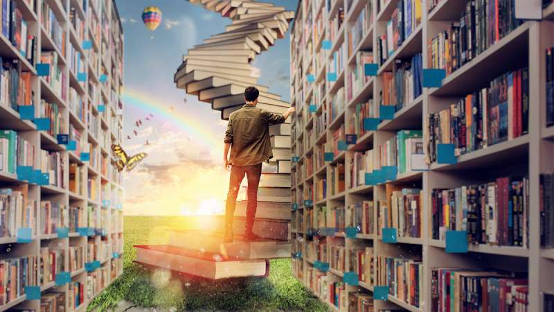 Inside of a library, a student is walking up a staircase of books leading up into the sky.