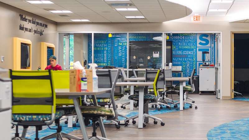 A student sitting at a table in the "makerspace" area of the STEM Center, which consists of several open table workspaces.