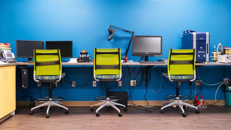 Three chairs in front of the desk of the Nano Technology Lab in the STEM Center. Various equipment is sitting on the desktop, including computer monitors, and an electron microscope
