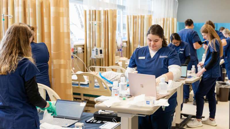 A nursing lab inside of NTC's Center for Health Sciences. Five patient beds are visible, with students attending each.
