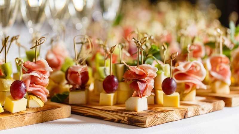A table full of appetizers with cheese, grapes, and meat held together with tooth picks.