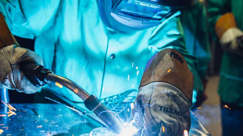 Upclose shot of a student welding. Blue sparks are flying.