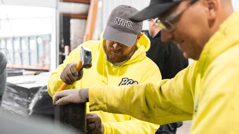 Two apprentices wearing safety gloves work together with tools on a project.