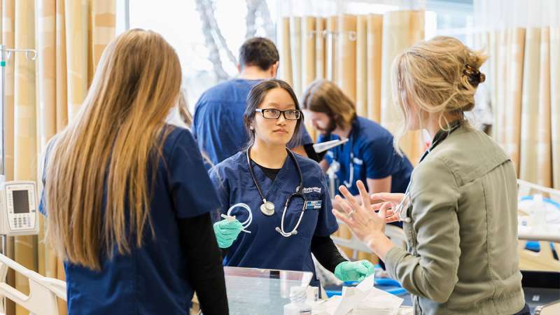 Two NTC Nursing students listening to an instructor inside of a medical classroom.