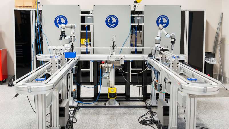 An electromechanical capstone station featuring conveyor belts, collaborative robot arms, and various sensors. The setup is framed by equipment labeled with Northcentral Technical College branding, emphasizing automation and fluid power training in a modern lab environment.