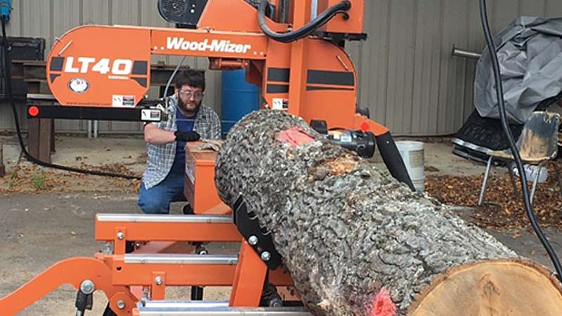 A man using a Wood-Mizer LT40 portable sawmill on a log outdoors.