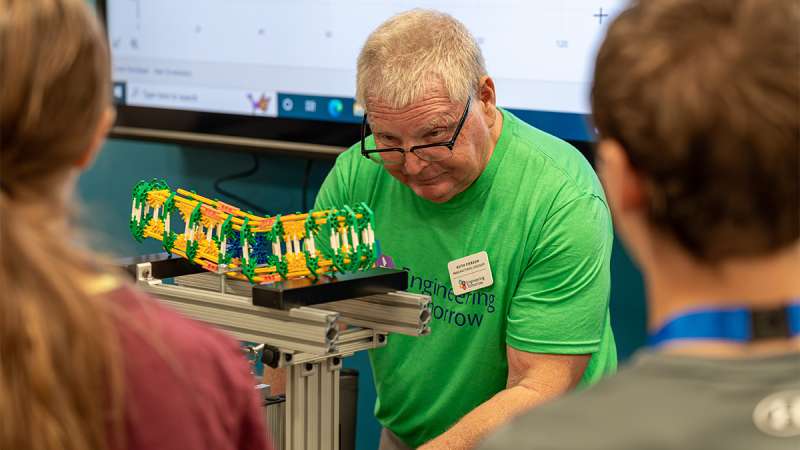 An instructor in a green shirt demonstrates a bridge model to students during an engineering workshop.