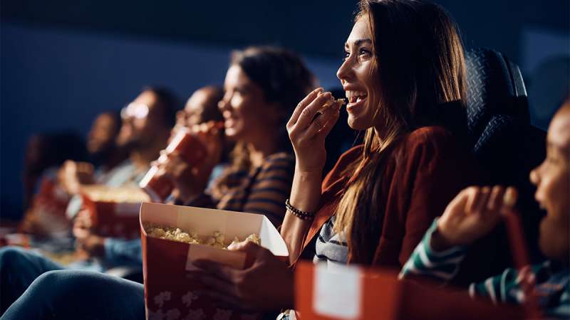Audience enjoying popcorn and laughing together while watching a movie in a darkened theater.