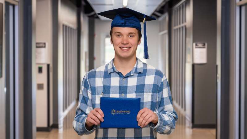 Mike smiling while wearing his graduation cap and holding his diploma.