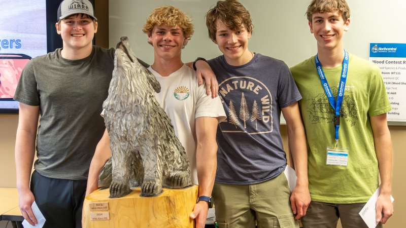 Four students pose with Wood Olympics Trophy