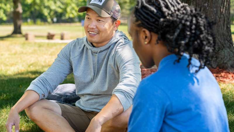 Two students talking in the courtyard. One is smiling.
