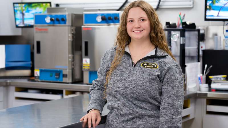 Martina smiling while standing by a stainless steel counter inside Mullins Cheese.