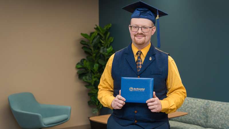Luke smiling while wearing his graduation cap and holding up his diploma