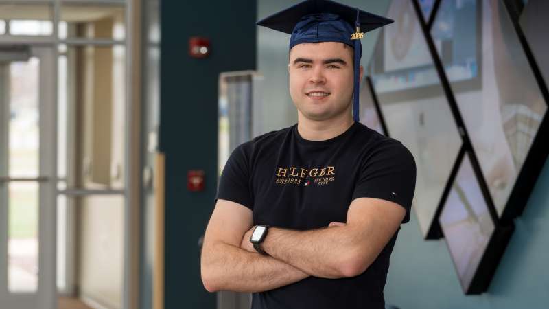 Mick smiling while wearing his graduation cap and his arms crossed.