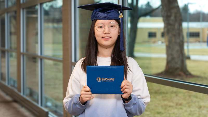 Susie smiling while wearing her graduation cap and holding up her diploma
