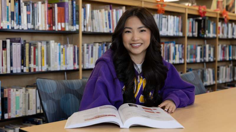 Samyris seated at a library table with a textbook open in front of her
