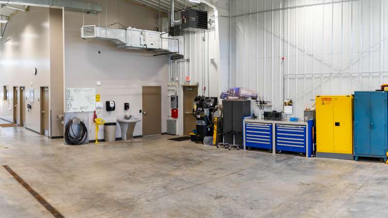 CDL Training Center training bay with concrete floor, high white walls, overhead lights; row of tool cabinets, lockers, workbenches, and service carts along wall.