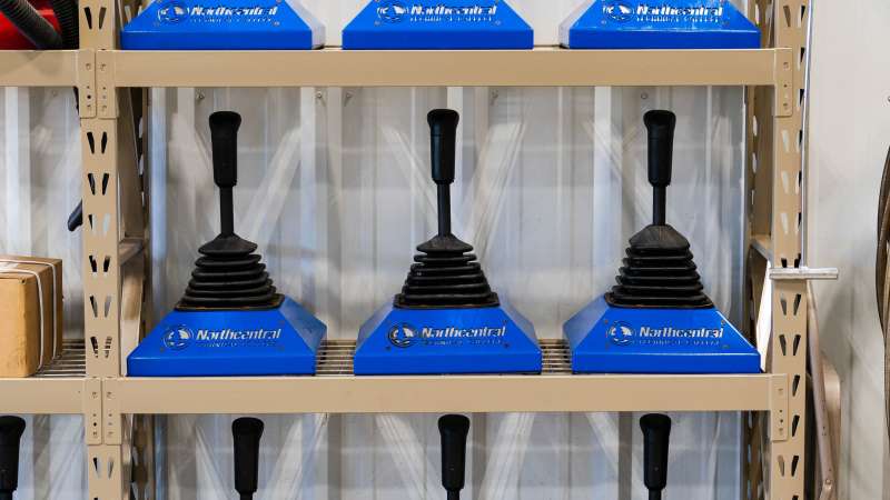 Practice truck shifters used in VR driving training, lined up on shelves and mounted on blue Northcentral Technical College bases.
