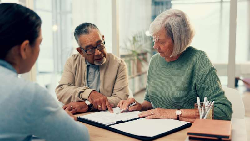 Older couple meeting with a professional at a sunlit office desk, reviewing documents together