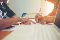 A man is sitting down at a table with another person writing down his information on a registration form