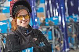 A student apprentice standing with her arms crossed in front of mechical equipment