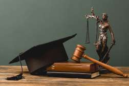 A graduation hat sits on top of a law book next to a gavel and lady justice