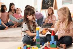 Children are playing with toy blocks and having a story read to them by a child care worker