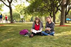 Two students sit together on the grass with school books in the Wausau Campus Courtyard