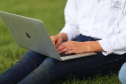 A student is sitting on the grass typing on an Apple Macbook Pro laptop.