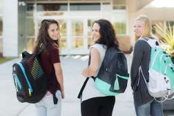 Three students wearing backpacks are walking towards the front entrance of Northcentral Technical College