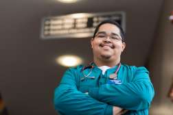 Juanmanuel standing at the top of the stairs, smiling, with arms crossed, in the CHS building on the Wausau Campus.