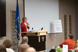 Dr. Lori Weyers stands in front of a podium giving a speech in front of an audience at Northcentral Technical College.