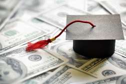 A black college graduation cap with red tassels sits on top of one-hundred-dollar bills.