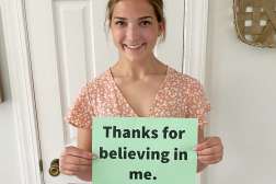 An NTC student holds up a small sign with "Thanks for believing in me" written on it.