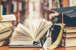 Several books, a laptop, and a graduation hat are stacked on top of a table inside of a library.