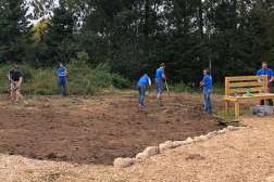 Several NTC employees are weeding through dirt by hand and with garden tools at the Monk Botanical Gardens.