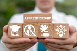 A man wearing a white shirt and blue tie is holding blocks with icons and one large block that says apprenticeship.