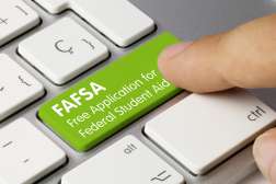 A finger presses down on a keyboard key that says "FAFSA free application for federal student aid".