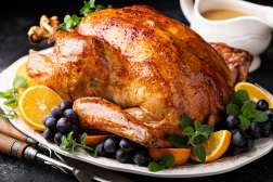 A roasted turkey on a plate surrounded by gravy and fruits.