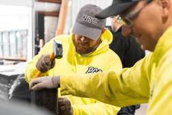 Two apprentices wearing safety gloves work together with tools on a project.