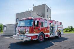 A red fire engine labeled Northcentral Technical College is parked on a blacktop surface near a multi-story training facility under a clear blue sky.
