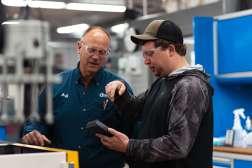 Two manufacturing workers collaborate, examining a component in a high-tech industrial workshop setting.