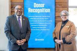 Two presidents from organizations smiling in front of a donor recognition sign at Northcentral Technical College.