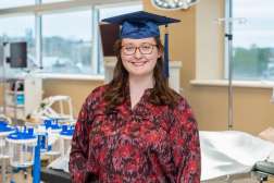 Adriana smiling while wearing her graduation cap while standing inside a lab in the Center for Health Science