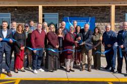 A large group of smiling people participates in a ribbon-cutting ceremony.
