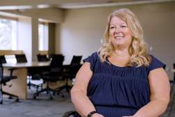 Amy sitting in a modern conference room, wearing a dark blue top.