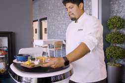 A culinary student serving food with help from an AI robot.