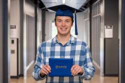 Mike smiling while wearing his graduation cap and holding his diploma.