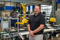 Dustin Van De Weerd smiling with arms crossed while standing inside the Industry 4.0 Smart Manufacturing Lab