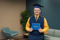 Luke smiling while wearing his graduation cap and holding up his diploma